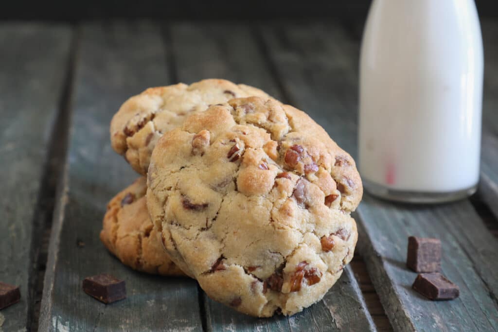 Two chunky chocolate chip cookies on top of each other and one leaning against them.