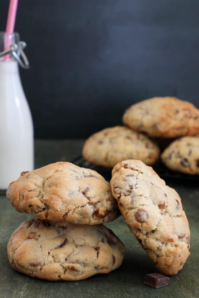 Two cookies stacked and one leaning against them with three other cookies in the back with a glass bottle of milk.