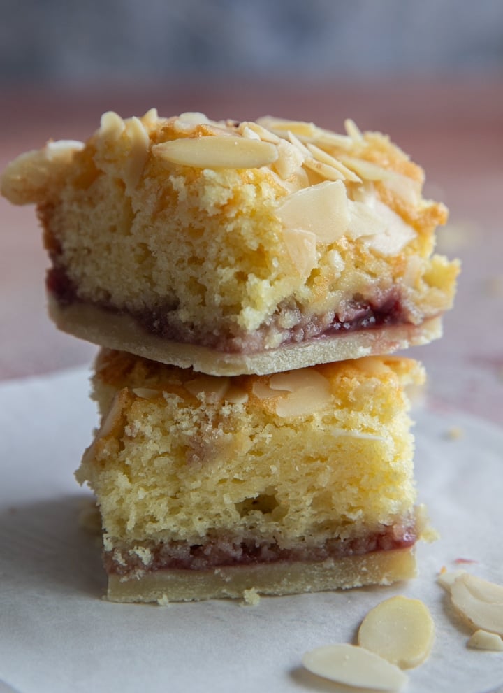 Two squares of bakewell bars one on top of the other on a parchment paper sheet.