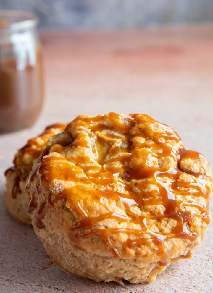 Two caramel and apple scones with a jar of caramel sauce in the back.