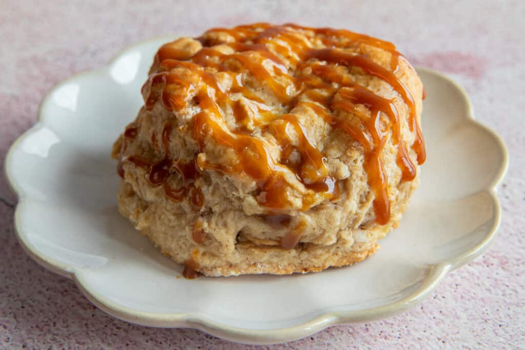 An apple caramel scone drizzled with caramel sauce on a white plate.