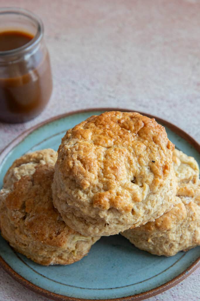 Three scones on a green plate with a jar of caramel sauce on the top left side.