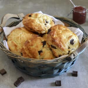 Chocolate chip scones in a blue basket with chocolate chunks scattered around it.