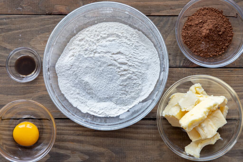 Ingredients to make chocolate cut out cookies in separate bowls.