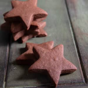 Two chocolate cookie stars on a green board and three stars stacked behind them.