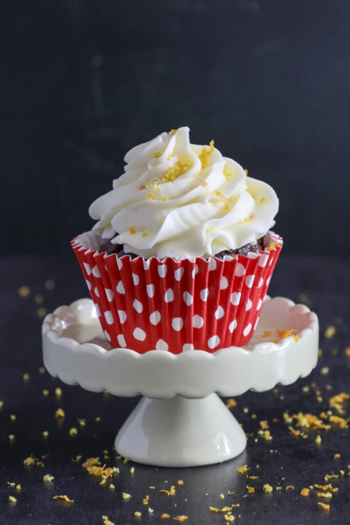 A chocolate orange cupcake in a red cupcake holder on top of a white cake stand.