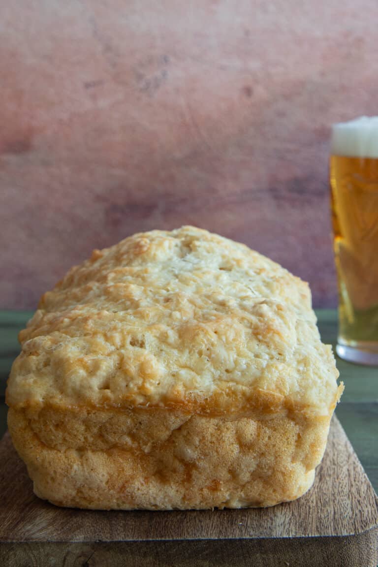 Cheesy beer bread on a wooden board with a glass of beer in the back.