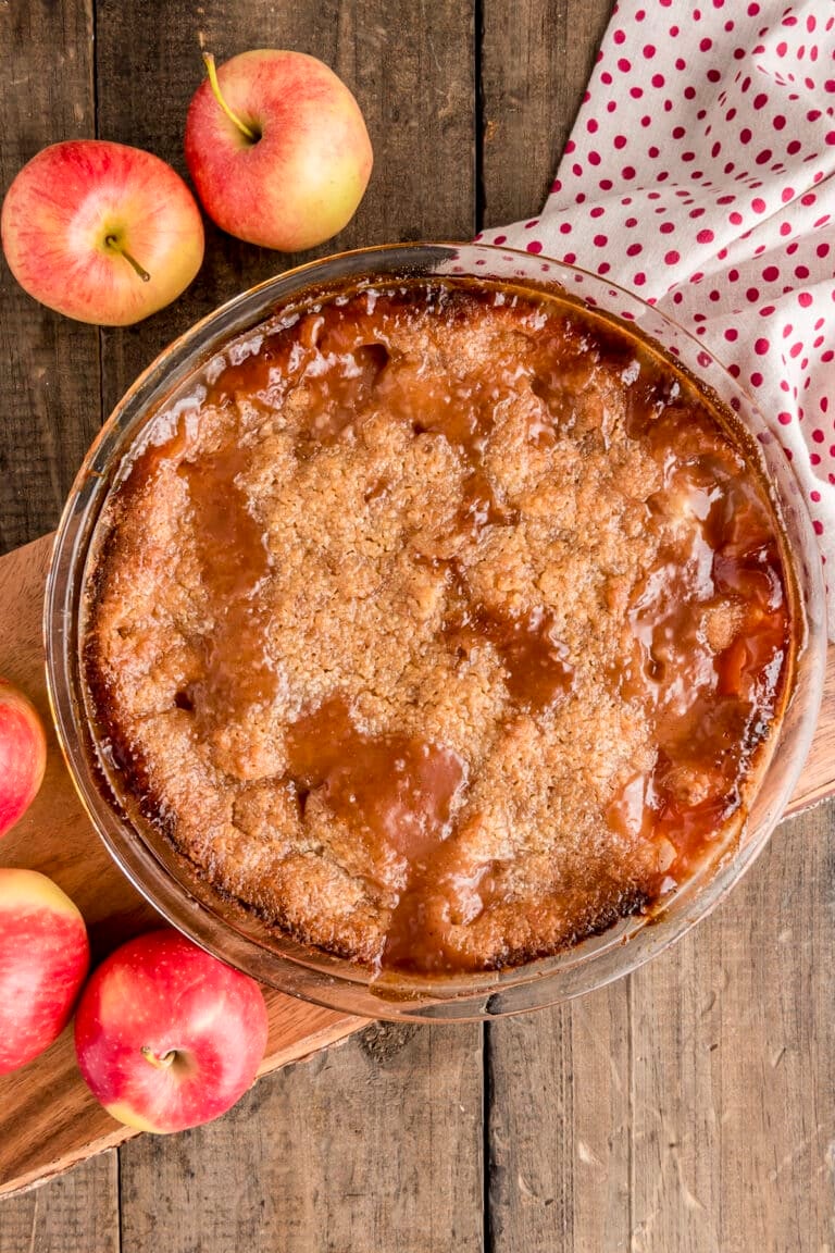 Apple pie in a pie dish with apples around it.
