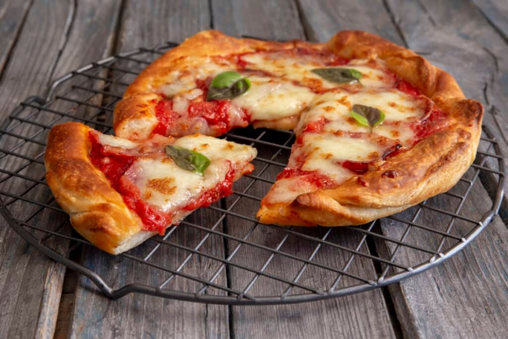 An air fryer pizza with a slice cut on a cooling rack.