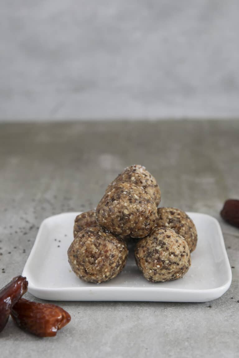 Six energy balls stacked on top of each other on a square white plate.