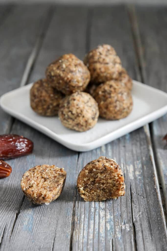 Five energy balls stacked on a square white plate with one ball cut in half in front.