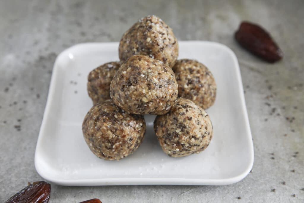 Six salted caramel energy balls stacked on top of a square white plate.