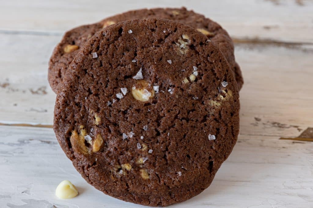 One crunchy white chocolate chip cookie standing leaning against other cookies stacked.