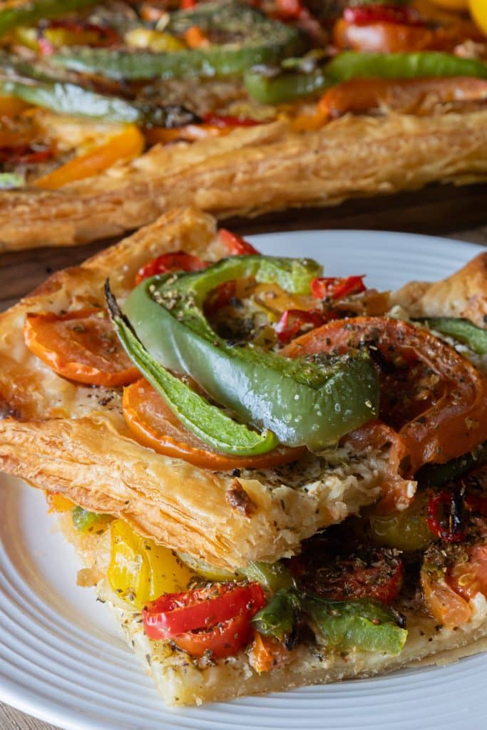Two slices of tomato and mascarpone tart on a white plate with the rest of the tart in the back.
