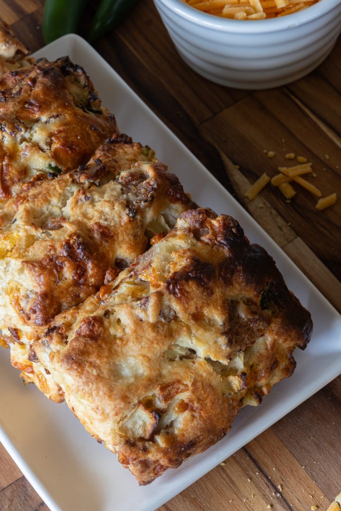 Jalapeno apple sausage and cheddar biscuits laid on a white plate on top of a wooden board.