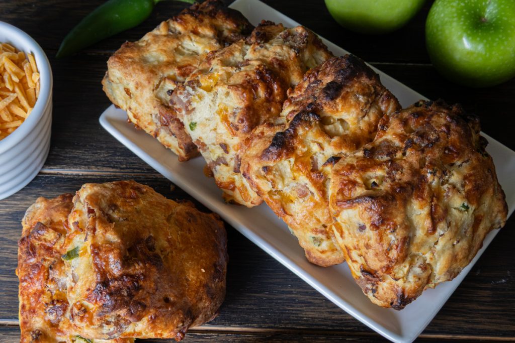 Four jalapeno biscuits on a white dish with two laid on a wooden board.