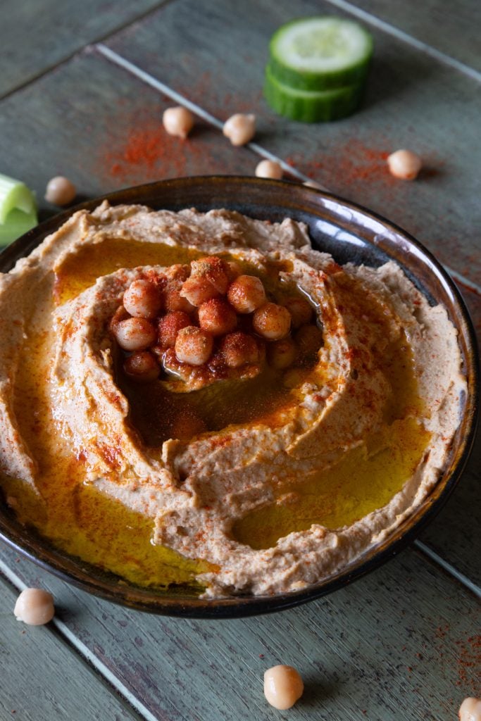 Hummus topped with chickpeas and olive oil inside a dark bowl.