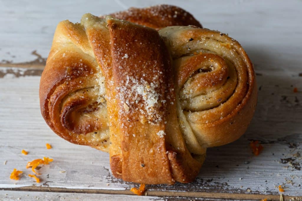 Blood orange cardamom bun on a white board leaning against another bun.