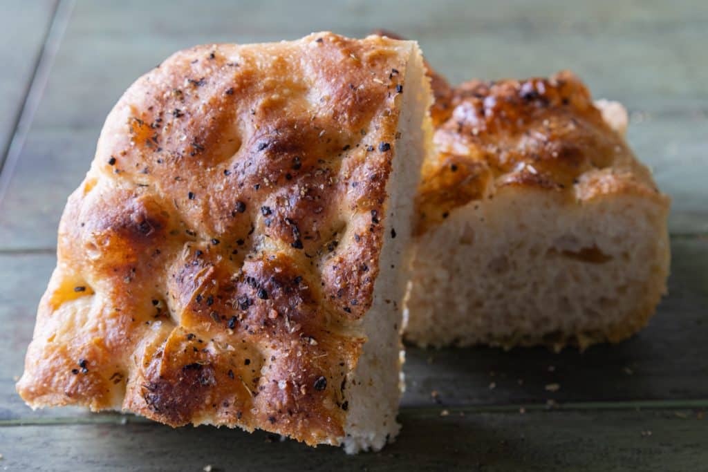 Two pieces of Sourdough discard focaccia on a green wooden board.